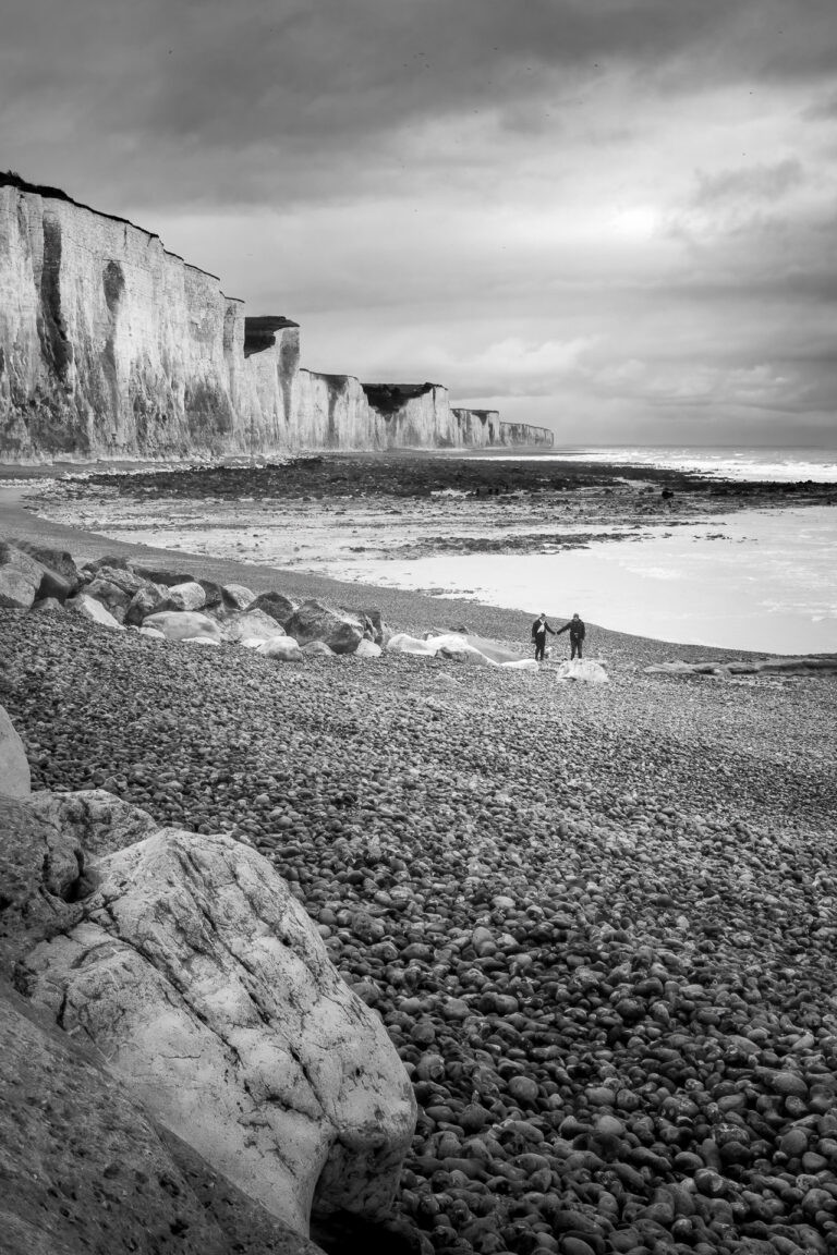 Two walkers on the shingle beach below the chalk cliffs of Ault, France