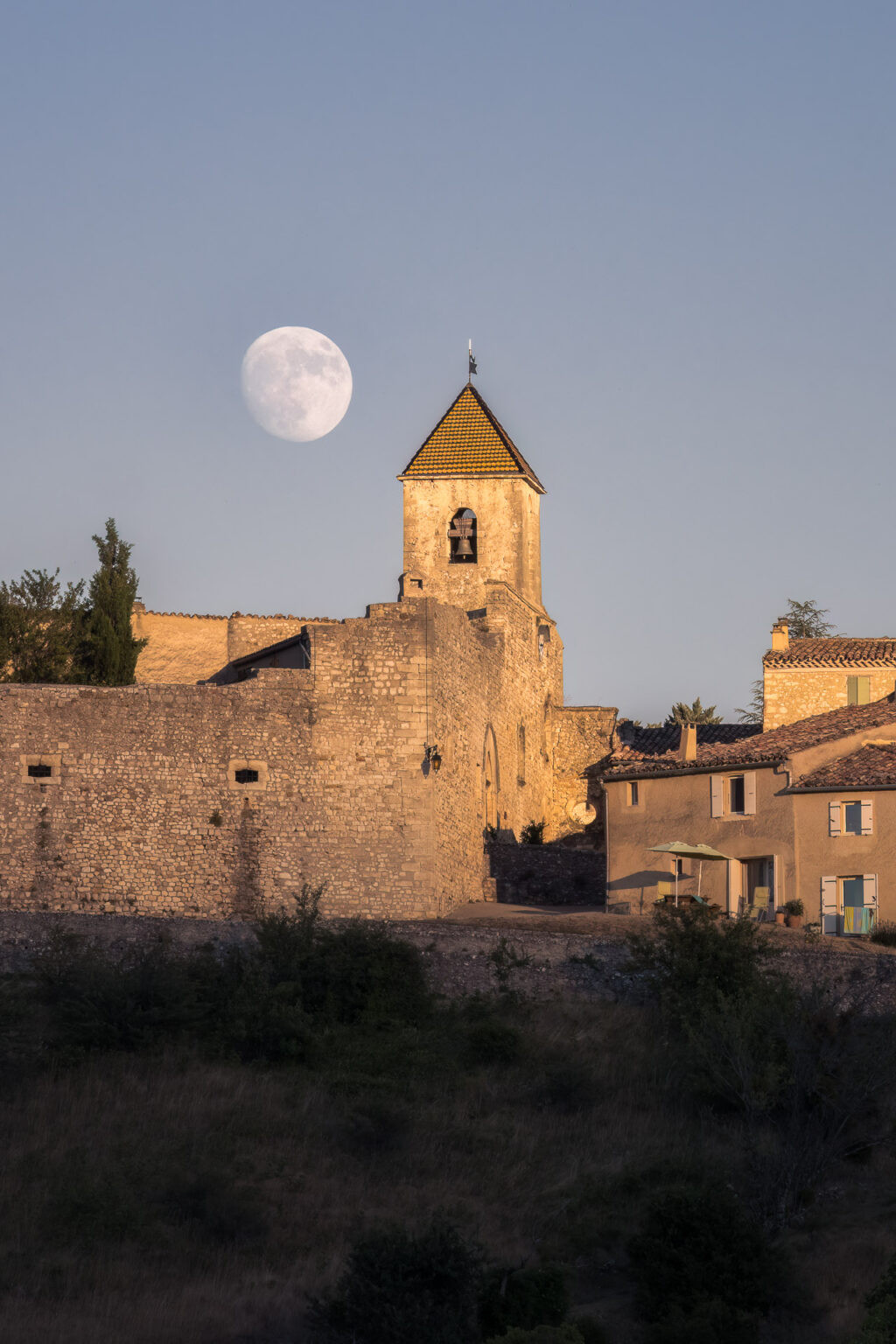 Le clocher d’Aurel à côté d’une lune presque pleine au crépuscule, Vaucluse, France.