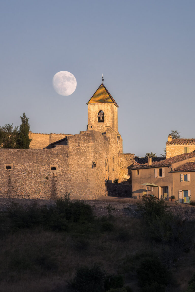 Der Kirchturm von Aurel neben dem fast vollen Mond in der Abenddämmerung, Vaucluse, Frankreich.